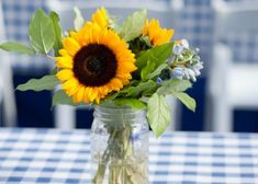 a sunflower in a mason jar on a table with blue checkered tablecloth