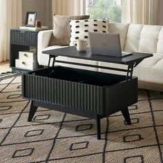 a living room with a couch, coffee table and laptop on top of it in front of a window