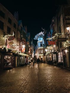 people are walking down the street in an old town at night with christmas lights on