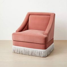 an upholstered pink chair with fringe trim around the legs and foot rests on a wooden floor