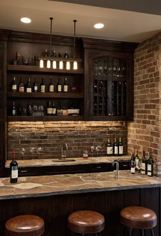 a home bar with stools and bottles on the wall behind it in front of brick walls