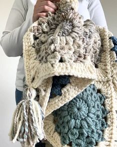 a woman is holding a crocheted blanket with tassels