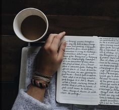 a person is reading a book and holding a cup of coffee