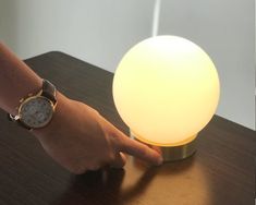 a person's hand is pointing at a light on a wooden table with a clock