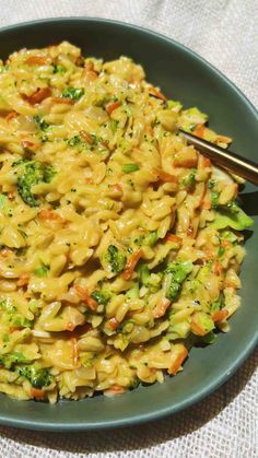 a bowl filled with pasta and broccoli on top of a table cloth next to a fork