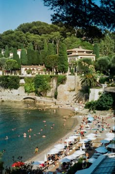 many people are on the beach and in the water near some buildings with trees around them