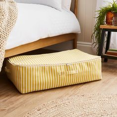 a yellow and white striped storage bag sitting on the floor in front of a bed