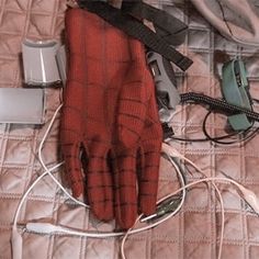 a pair of red gloves sitting on top of a bed next to headphones and cords