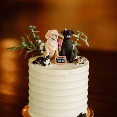 two dogs and three cats are sitting on top of a white cake with greenery