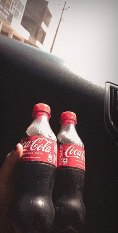 two bottles of coca - cola sitting in the back seat of a car, being held by someone's hand