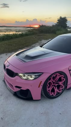 a pink car parked on top of a sandy beach next to the ocean at sunset