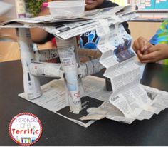 two children are sitting at a table with newspapers on top of it and one boy is smiling