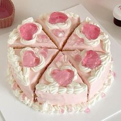 a cake with pink frosting and hearts cut into slices on a white plate next to cupcakes