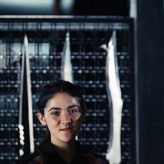 a woman is standing in front of some metal objects and looking at the camera with an intense look on her face