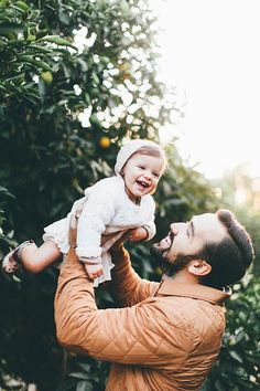 a man holding a baby up to his face in front of an orange tree with leaves