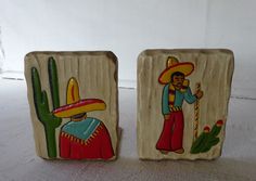 two wooden blocks decorated with mexican artwork and cactuses on the sides, one is holding a candy cane