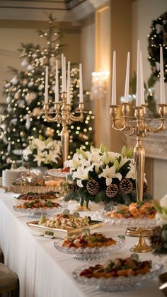 a table with candles and food on it in front of a christmas tree that is lit