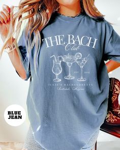 a woman wearing a t - shirt that says the beach club with two glasses of wine