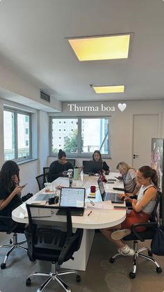 a group of people sitting around a table with laptops on top of it in an office