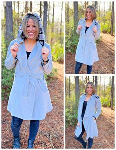 a woman is posing in the woods wearing a gray coat and blue jeans with her hood up