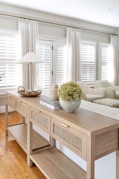 a living room with white couches and wooden table in front of the window covered by curtains