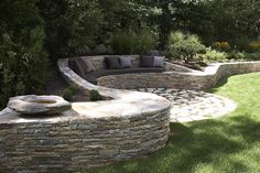 an outdoor seating area in the middle of a garden with stone walls and green grass