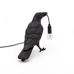 a black bird lamp sitting on top of a white table next to a light bulb