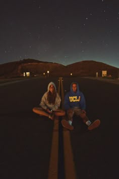 two people sitting on the ground with their skateboards in front of them at night