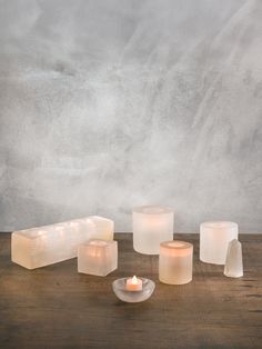 candles are arranged on a wooden table in front of a concrete wall and grey background