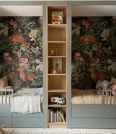 two children's beds in a room with floral wallpaper and wooden bookshelves