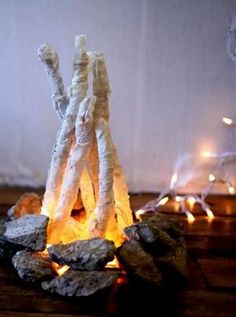 a fire pit made out of sticks and rocks on a wooden floor with lights in the background