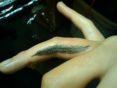 a woman's hand with a feather tattoo on her left thumb and the other arm