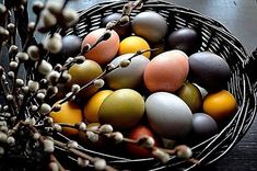 a basket filled with lots of different colored eggs next to some twig branches and berries