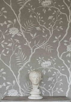 a white vase sitting on top of a table in front of a wallpapered tree