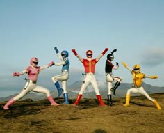 five people dressed in colorful costumes standing on top of a hill with their arms up