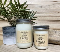 two candles sitting next to each other on top of a wooden table near a potted plant