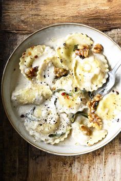 a white plate topped with ravioli covered in sauce and nuts next to a fork