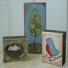 three wooden blocks with paintings of birds and eggs on them sitting on a table next to each other