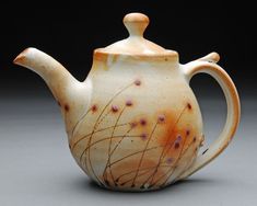 a ceramic teapot with brown and orange designs on it's side, sitting on a gray surface