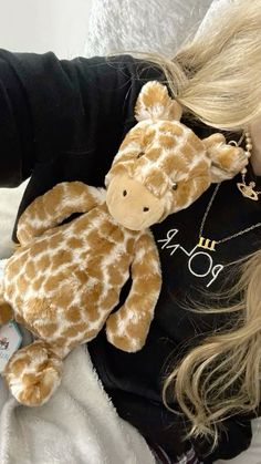 a blonde woman laying on top of a bed holding a stuffed giraffe in her lap