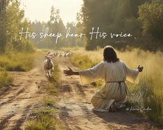 a person kneeling down in the middle of a dirt road with sheep walking behind them