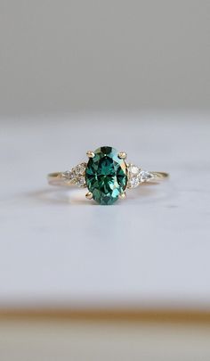 a green and white diamond ring sitting on top of a wooden table next to a wall