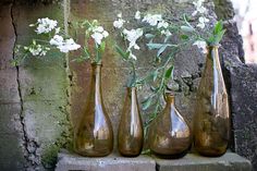 three vases with flowers in them sitting on a ledge next to a stone wall