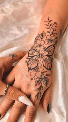 a woman's hand with tattoos and flowers on her left arm, sitting on a white sheet