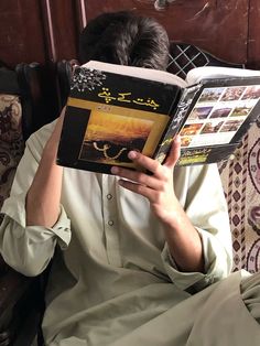 a man reading a book while sitting on a chair with his head in his hands