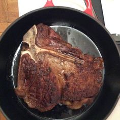 a steak in a skillet on a table next to an open book and utensils