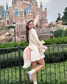 a woman posing for a photo in front of a castle with a stuffed animal on her shoulder