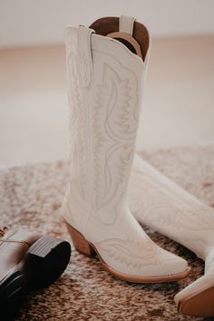 two pairs of white cowboy boots sitting on top of a rug next to each other