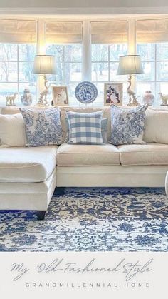 a living room filled with lots of furniture next to a large window covered in blue and white pillows