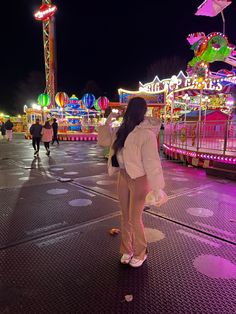 a woman standing in front of an amusement park at night with her back to the camera